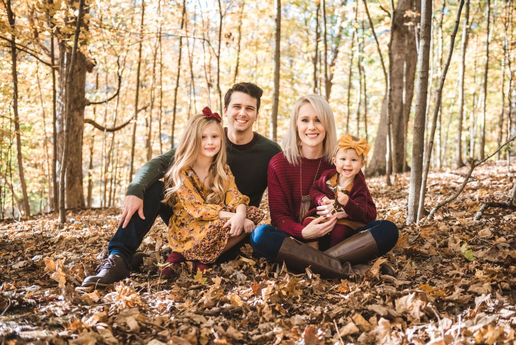 family sitting on leaves in woods for photo session